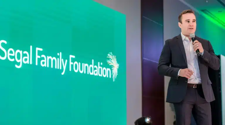 Andy Bryant holds a microphone in front of a large Segal Family Foundation backdrop
