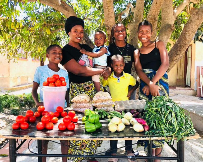 A Zambian family smiles behind a vegetable stand
