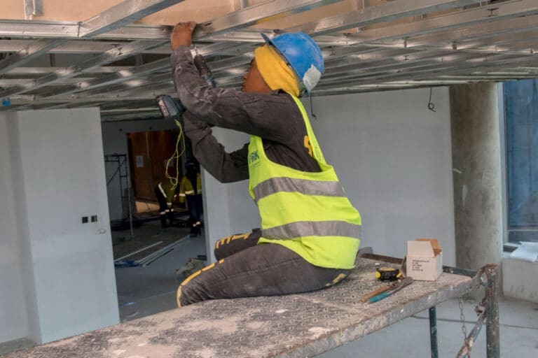 Une femme coiffée d'un casque utilise une perceuse au plafond.