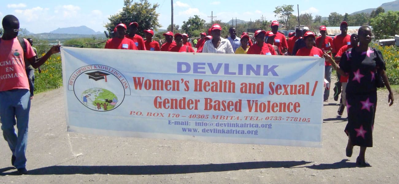 A group of Kenyans walk in a parade behind a Devlink banner