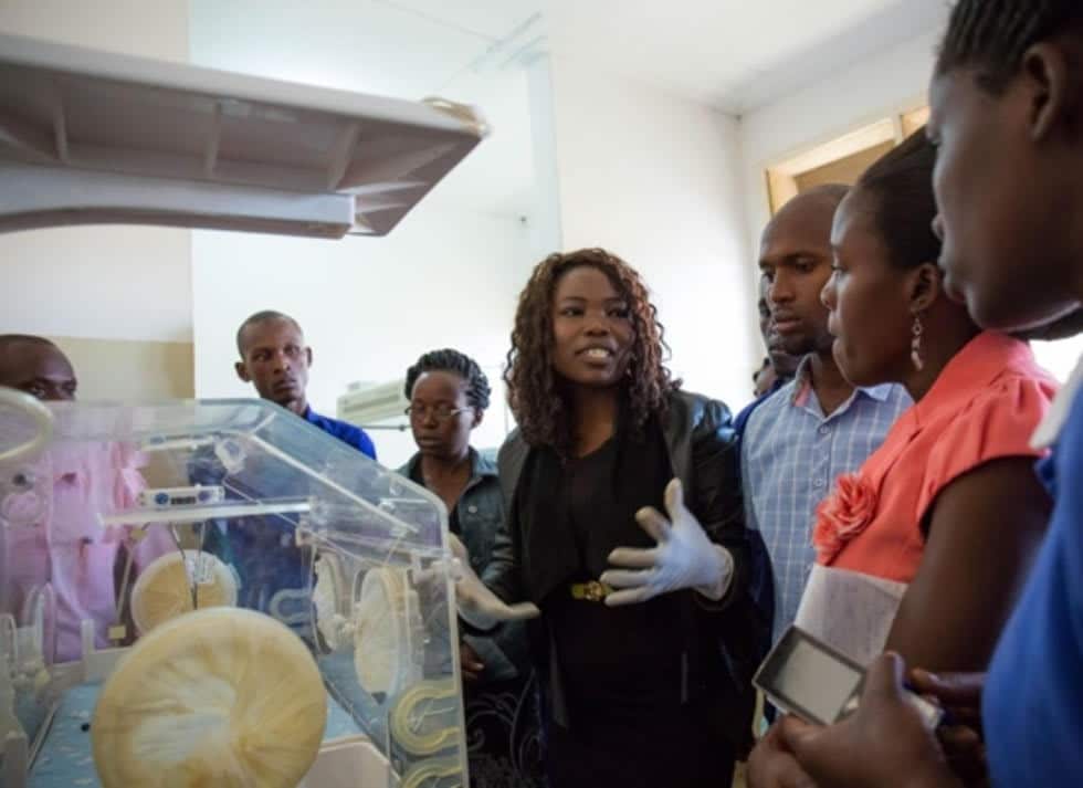 A group of African adults stand near a newborn incubator