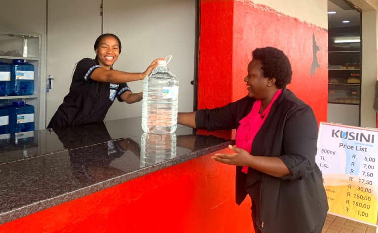Une femme donne de l'eau à une autre dans un kiosque de Kusini.