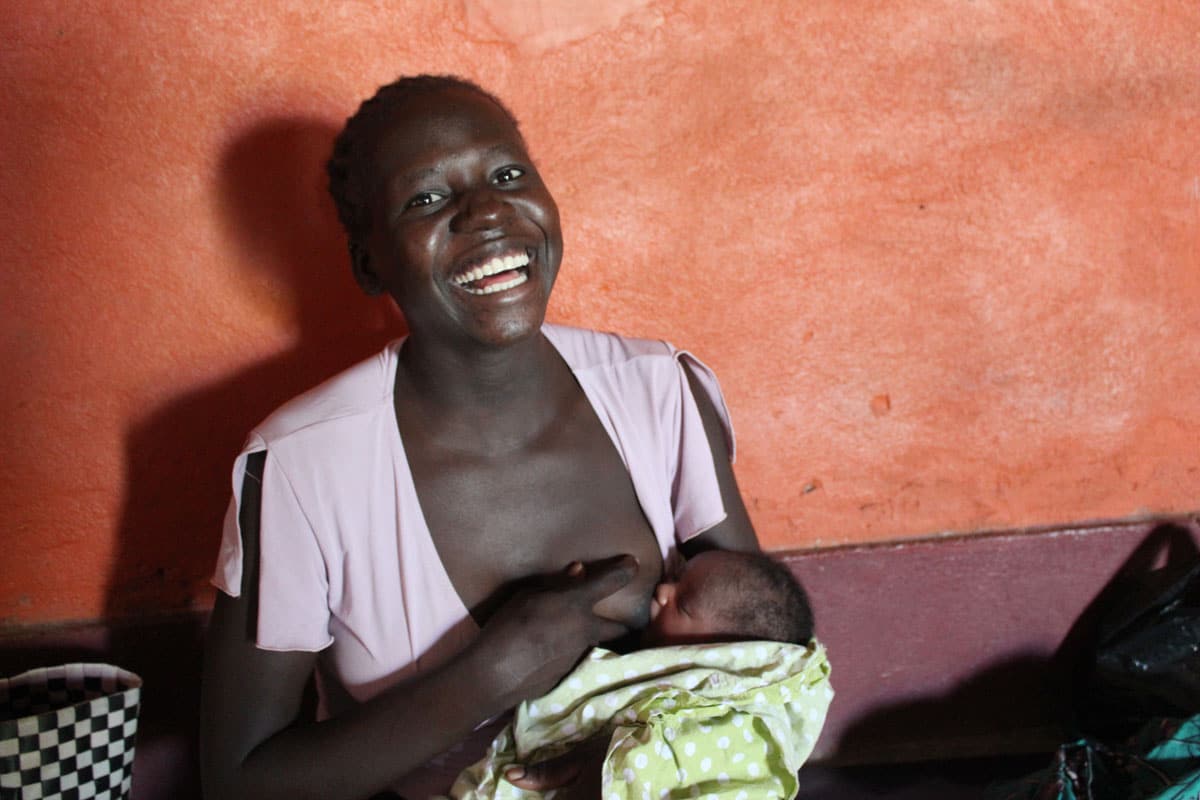 A laughing new mother breastfeeds her infant