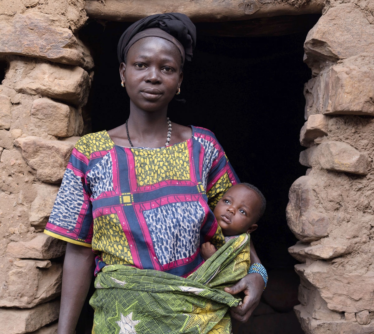 Une jeune mère avec son bébé se tient devant une porte en pierre.