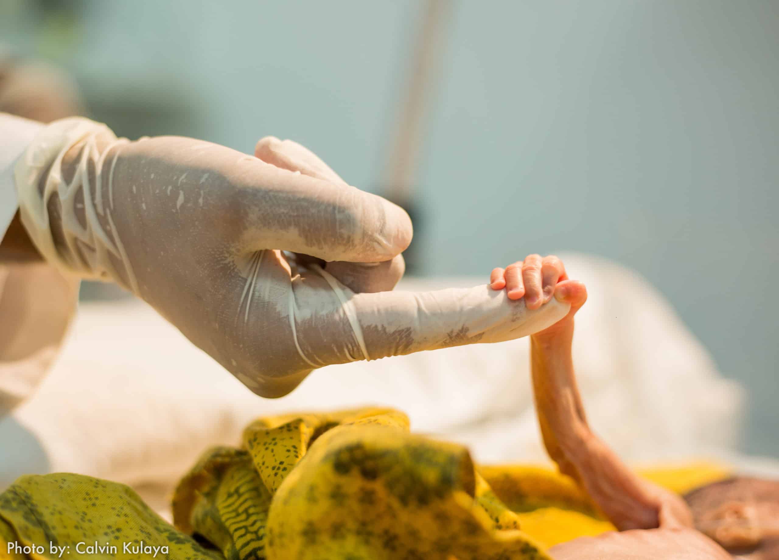 La main d'un bébé prématuré s'accroche à la main gantée d'un adulte.
