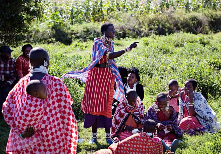 A woman stands and speaks to a pastoralist community