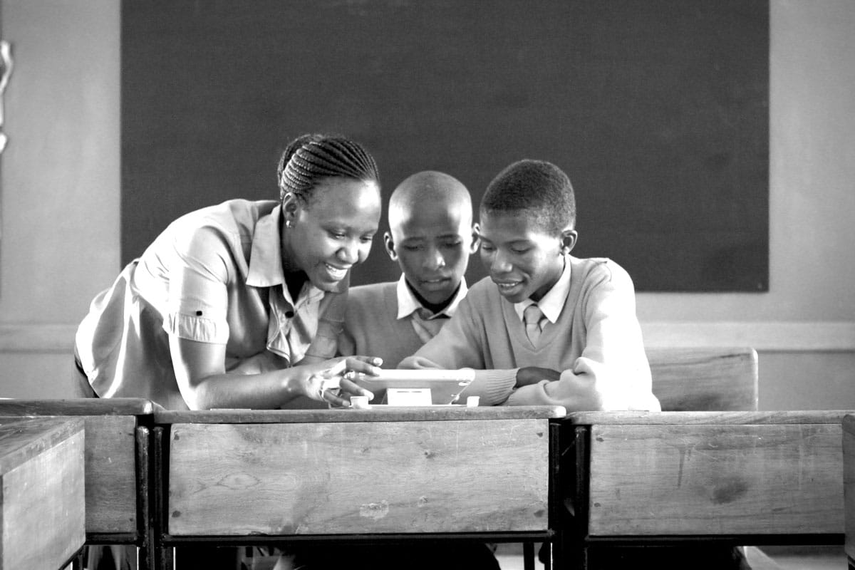A black-and-white image of three African students looking at a tablet