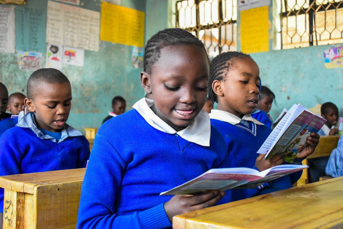 Des écoliers kenyans en pull bleu lisent à leur pupitre