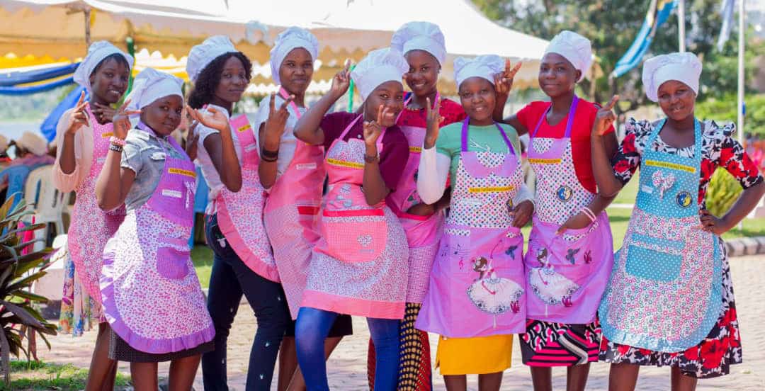 Nine domestic workers in colorful aprons pose with flair
