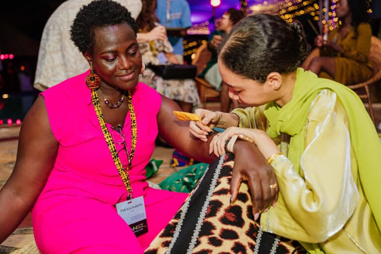 A woman paints henna on another seated woman