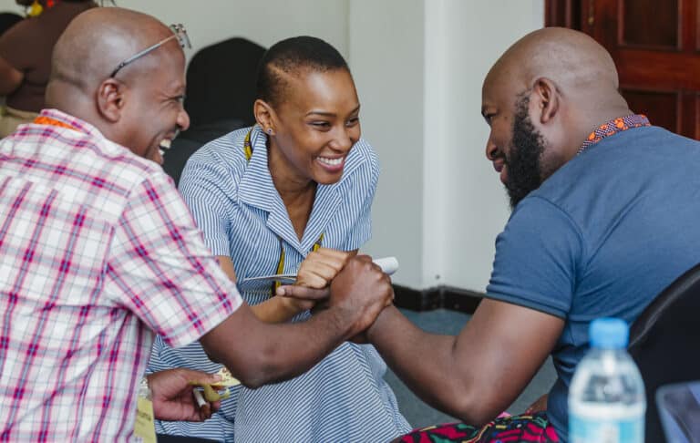 Three Tanzanian adults smile and hold hands
