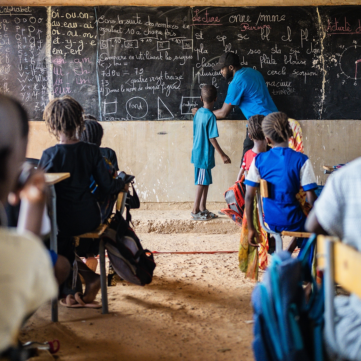 A teacher in Senegal instructs a student at a chalkboard in a classroom